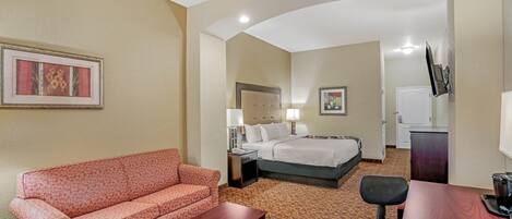 A hotel room with a sofa, a bed, a desk, and a television.