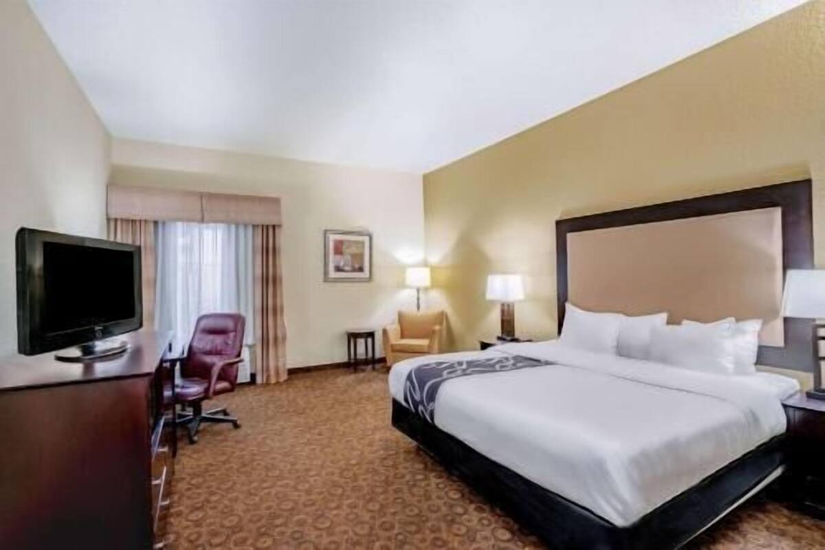 Una habitación de hotel con una cama, un escritorio con televisor, una silla y una lámpara.
