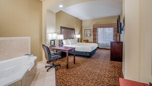 Ein Hotelzimmer mit Badewanne, Schreibtisch, Bett, Sessel und Fernseher.
