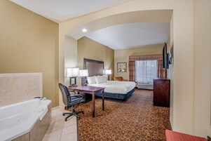 A hotel room with a bathtub, a desk, a bed, a chair, and a television.