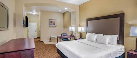 A hotel room with a large bed, a desk, a chair, and a small table with lamps.
