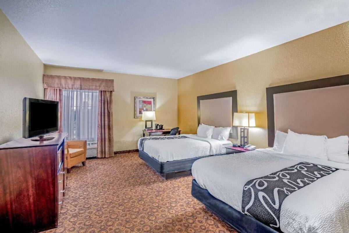 A hotel room with two beds, a TV, a desk, a chair, and a window with curtains.