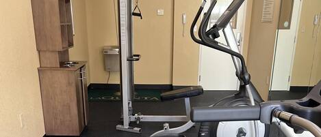 Zona fitness con attrezzi da allenamento, un armadio in legno e una porta con un cartello.