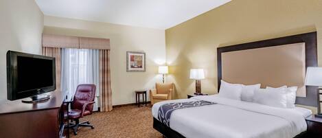 A hotel room with a bed, a TV, a desk, a chair, and a lamp.