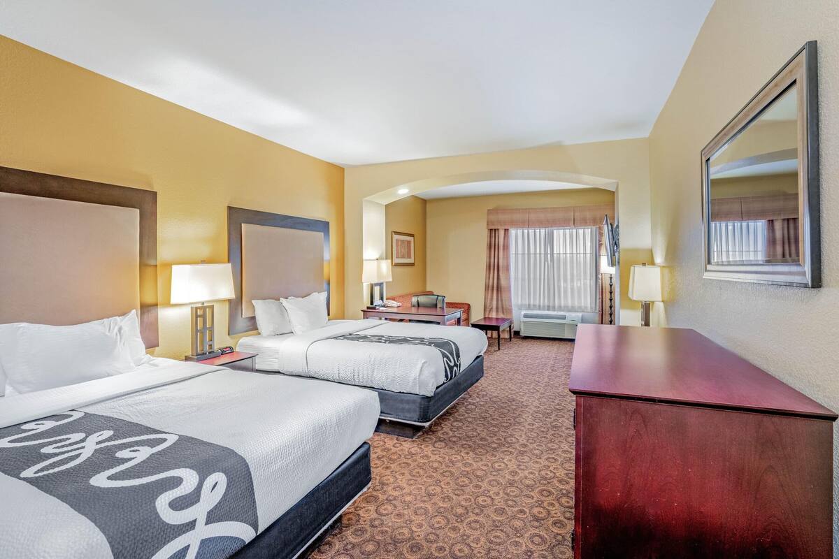 A hotel room with two beds, a desk, a chair, a dresser, and a large mirror.