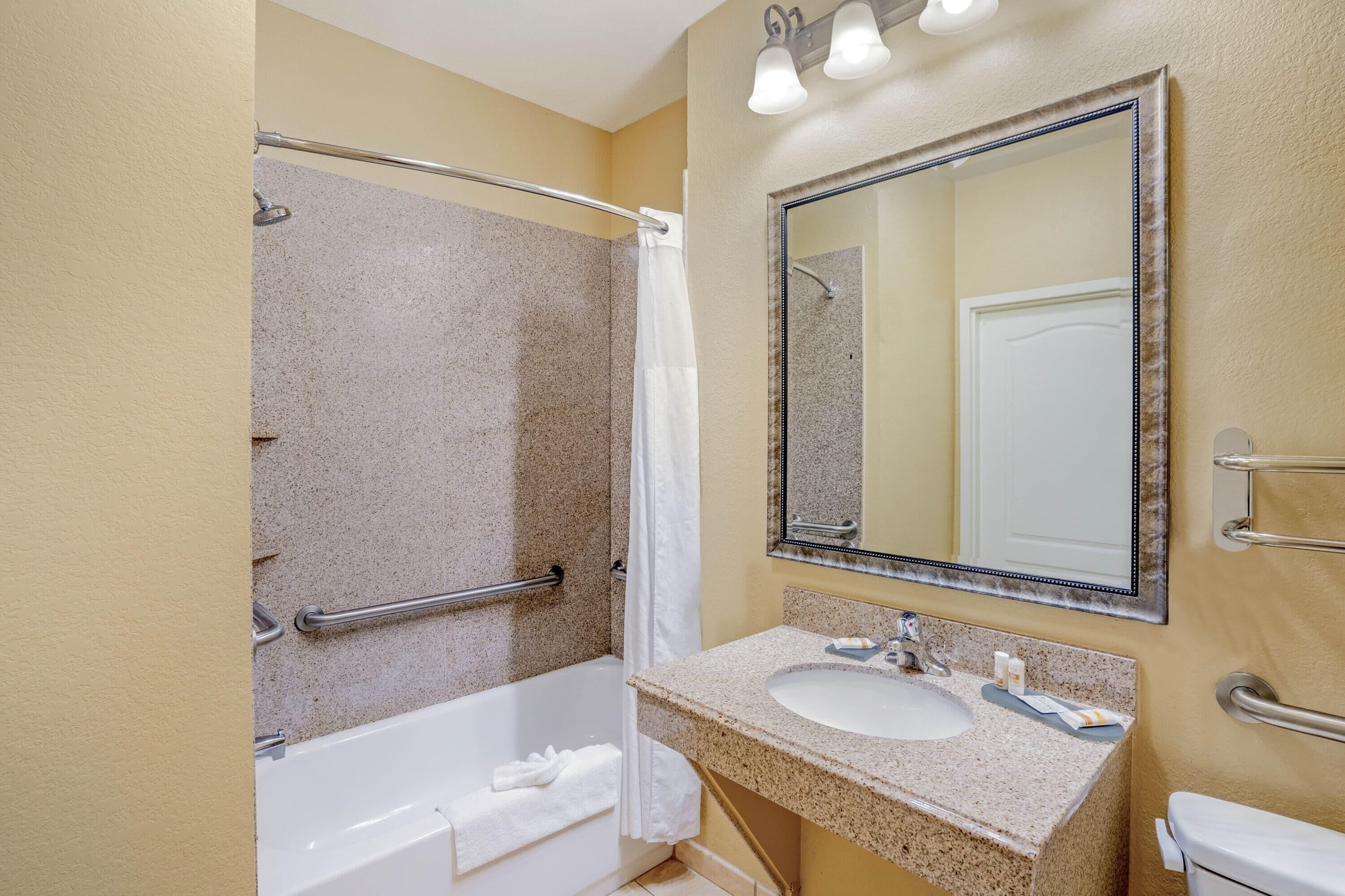 A bathroom with a bathtub, a sink, a mirror, and a shower area.