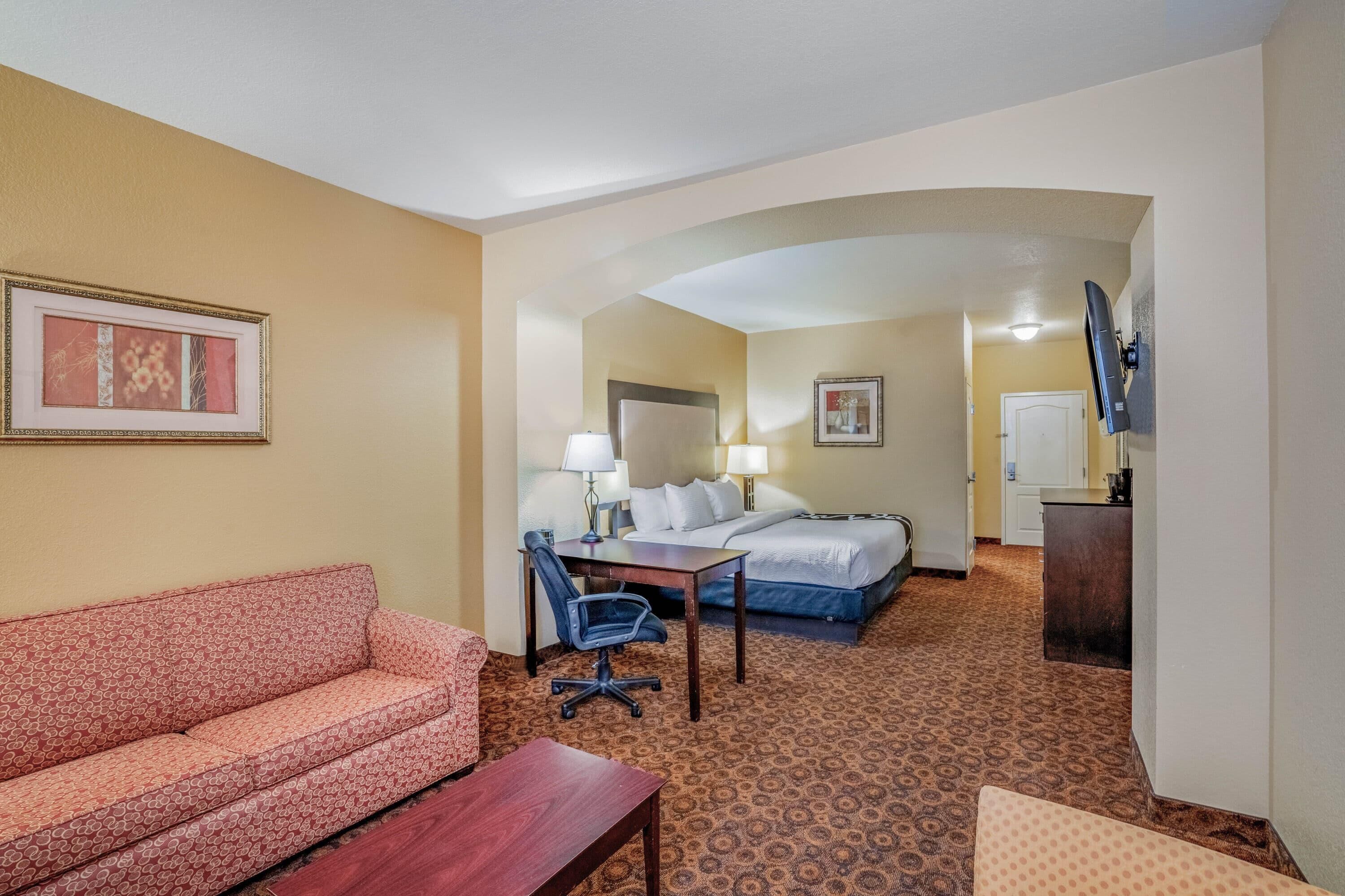 A hotel room with a sofa, a desk, a chair, a bed, and a TV.