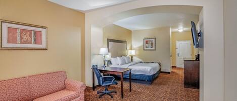 A hotel room with a sofa, a desk, a chair, a bed, and a TV.