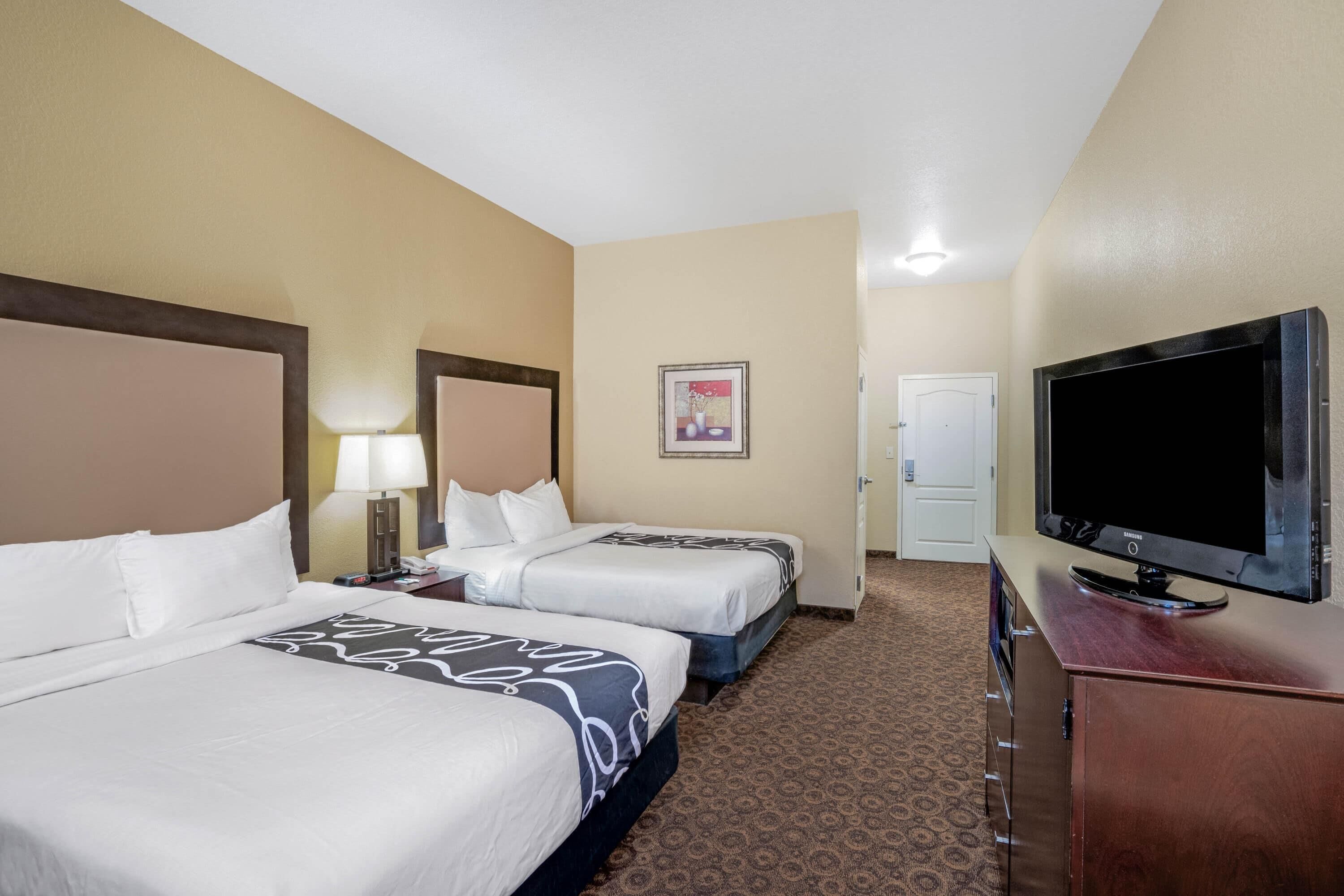 A hotel room with two beds, a TV, a desk, and a door.