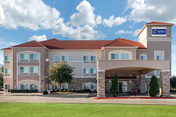 Un hotel de varios pisos con techo de tejas rojas, fachada de piedra y un cartel que indica que es un Comfort Inn & Suites.