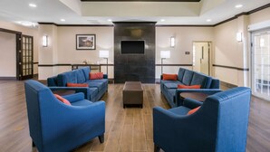 A lobby with blue sofas, a central ottoman, a flat-screen TV, and a stone fireplace. - Comfort Inn & Suites Cedar Hill Duncanville (Cedar Hill)