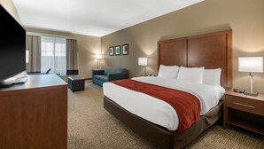 A hotel room with a large bed, a desk, a chair, a sofa, and two bedside lamps. - Comfort Inn & Suites Cedar Hill Duncanville (Cedar Hill)