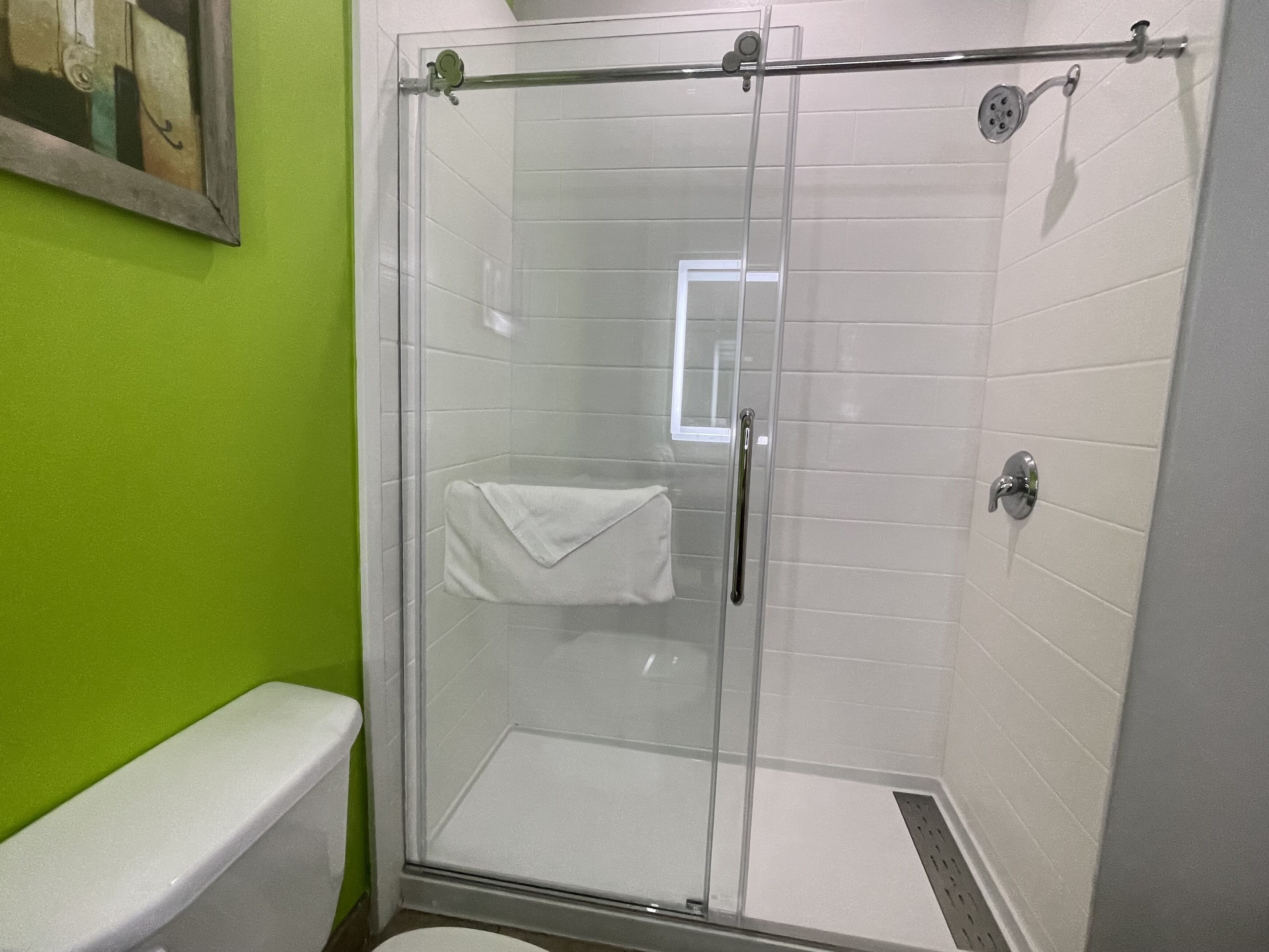Une douche fermée par des parois de verre, avec un mur recouvert de carreaux blancs, une porte en verre et une serviette blanche accrochée à la poignée de la porte.