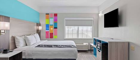 Een moderne hotelkamer met een bed, nachtkastje, televisie en kleurrijke wanddecoratie.