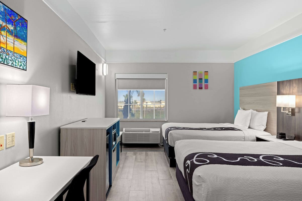 A hotel room with two beds, a desk, a TV, a window with a view, and a color-coded wall.