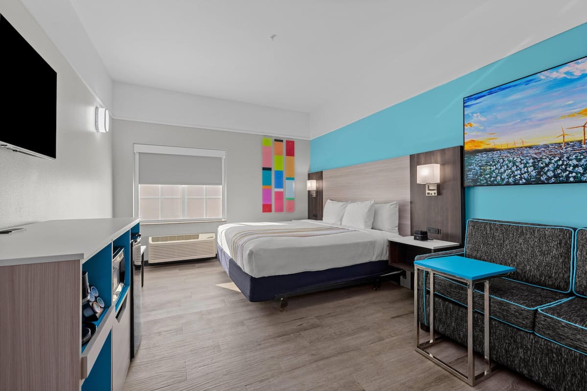 A hotel room with a bed, bedside table, TV, and a painting on the wall.