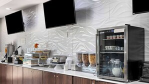 A modern kitchen with a stainless steel refrigerator, a coffee machine, and various food dispensers. - La Quinta Inn & Suites by Wyndham Raymondville (Raymondville)
