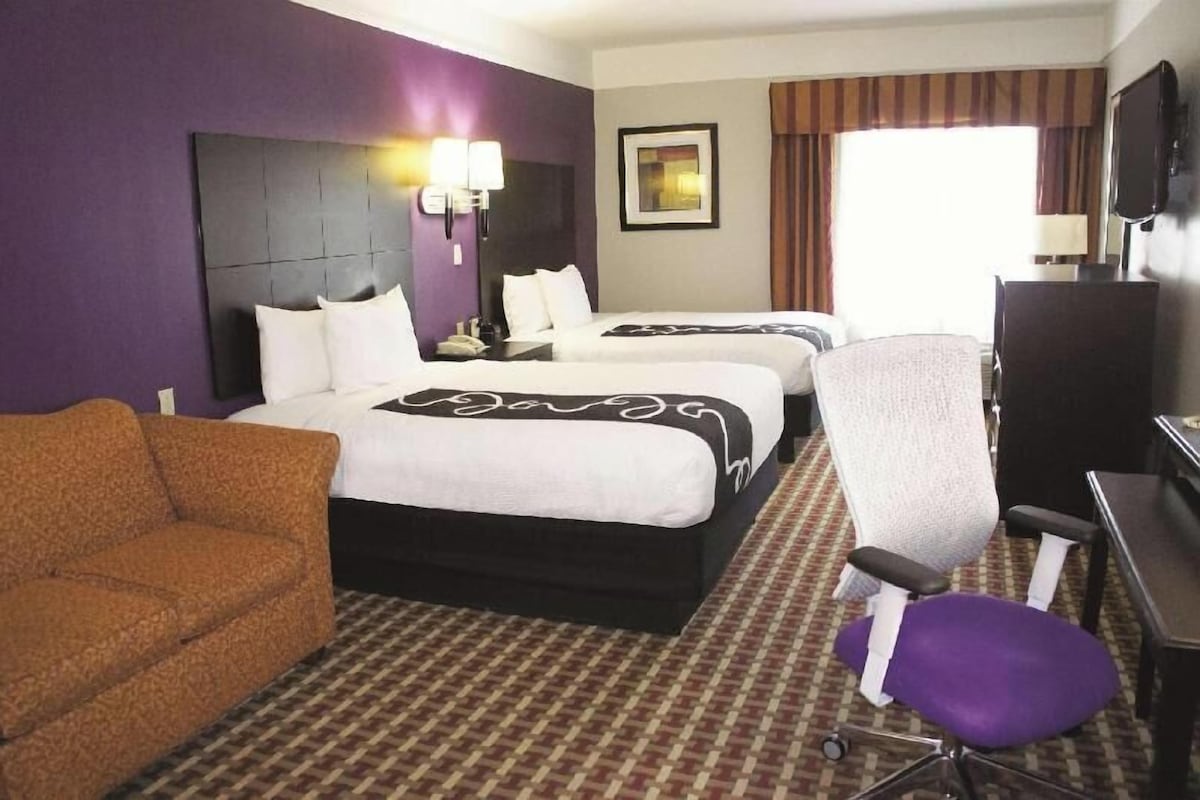 Una habitación de hotel con dos camas, un sofá, un escritorio y una televisión.