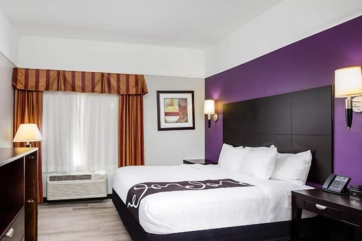 A hotel room with a bed, bedside tables, a TV, a window with curtains, and a wall-mounted picture.