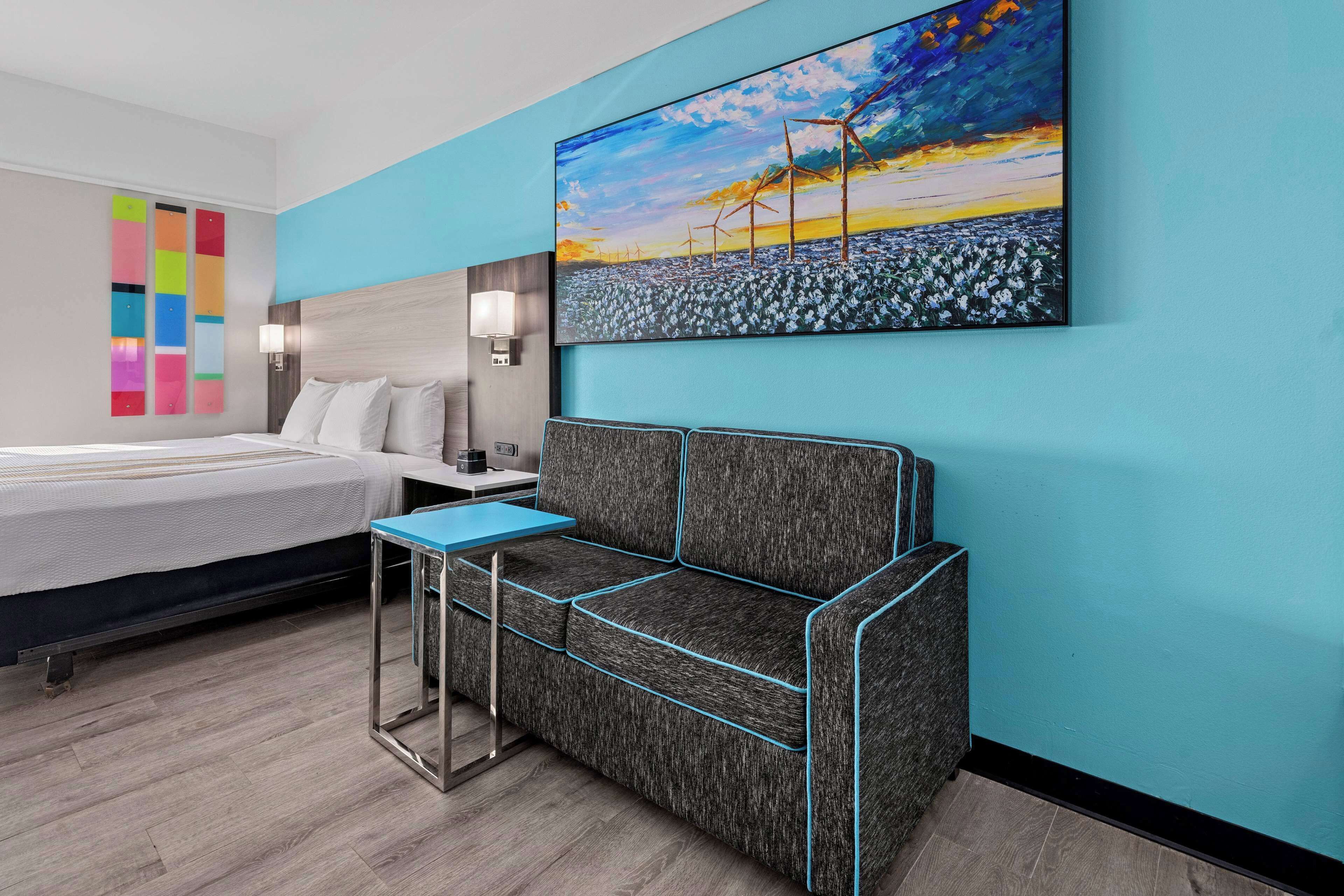 Una habitación de hotel moderna con una cama, un sofá, una mesita y un cuadro de un paisaje.