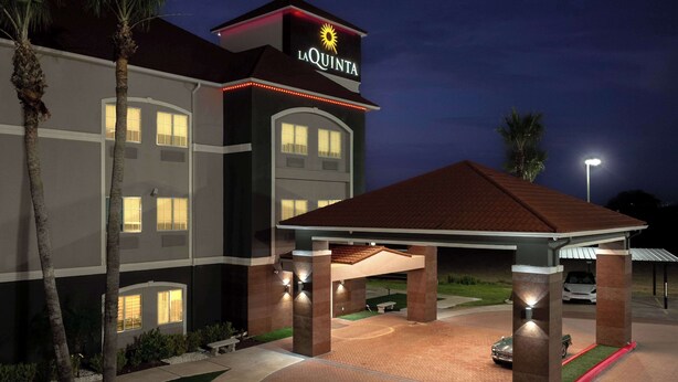 A hotel entrance with a covered area, palm trees, and a well-lit facade. - La Quinta Inn & Suites by Wyndham Raymondville (Raymondville)