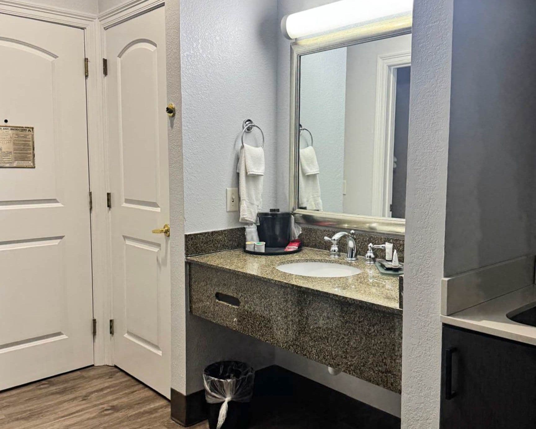 A hotel bathroom with a white sink, a mirror, a towel rack, and a trash bin.
