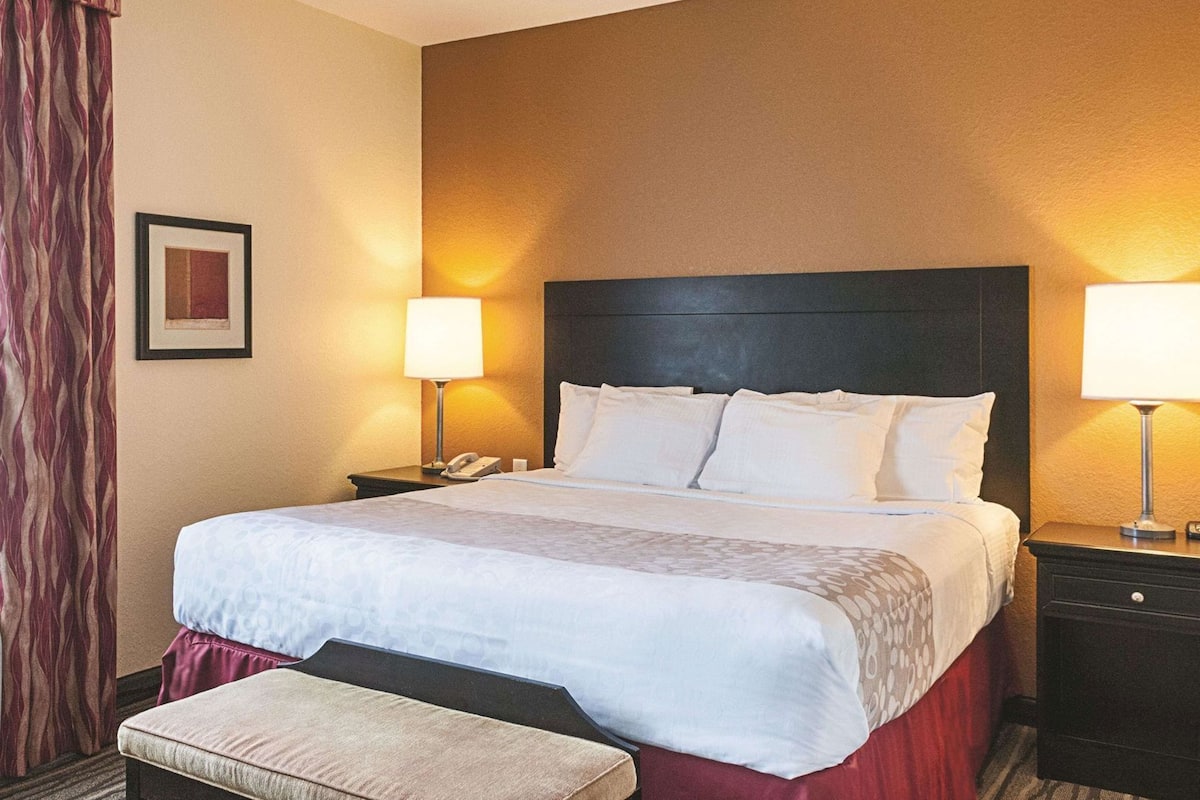 A hotel room with a large bed, two bedside tables, a bedside lamp, a telephone, a framed picture on the wall, and a window with curtains.