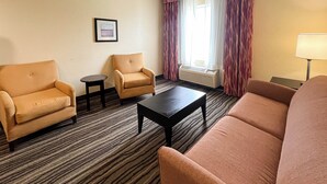 A hotel room with a sofa, two armchairs, a small table, a lamp, and a window with curtains.