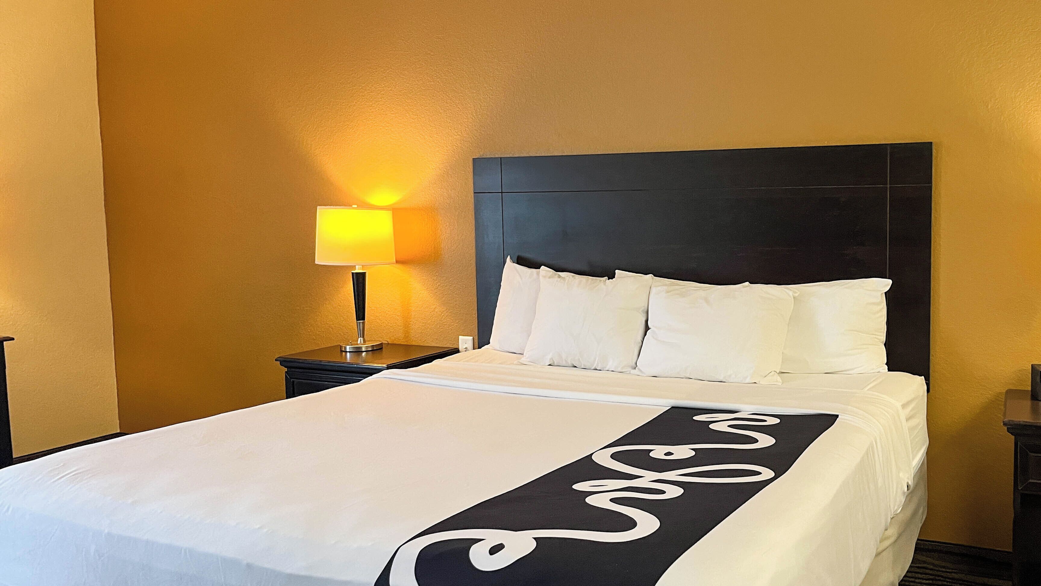 A hotel room with a bed, a nightstand with a lamp, and a headboard.