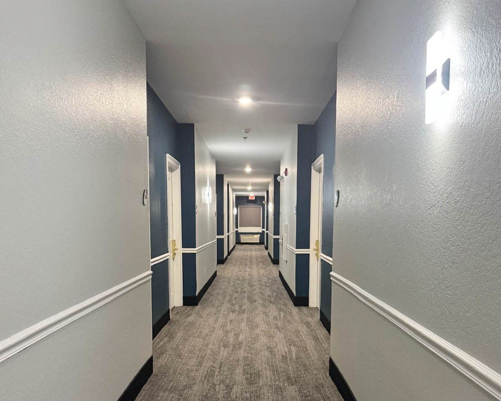 A corridor with doors on both sides, carpeted floor, and a light fixture on the ceiling.