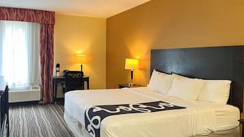 Ein Hotelzimmer mit einem Bett, zwei Nachttischlampen, einem Schreibtisch mit Stuhl, einem Fenster mit Vorhängen und einer Klimaanlage.