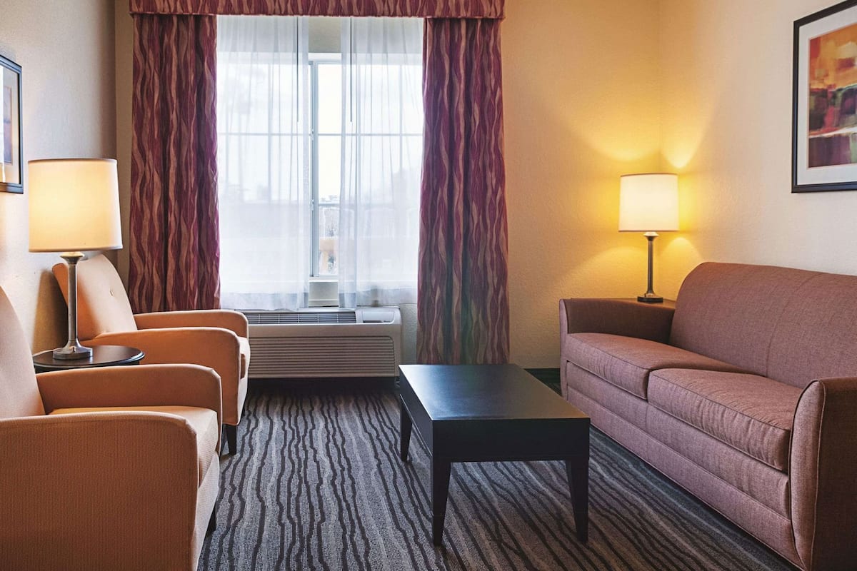 A hotel room with a sofa, two armchairs, a coffee table, a window with curtains, and two lamps.