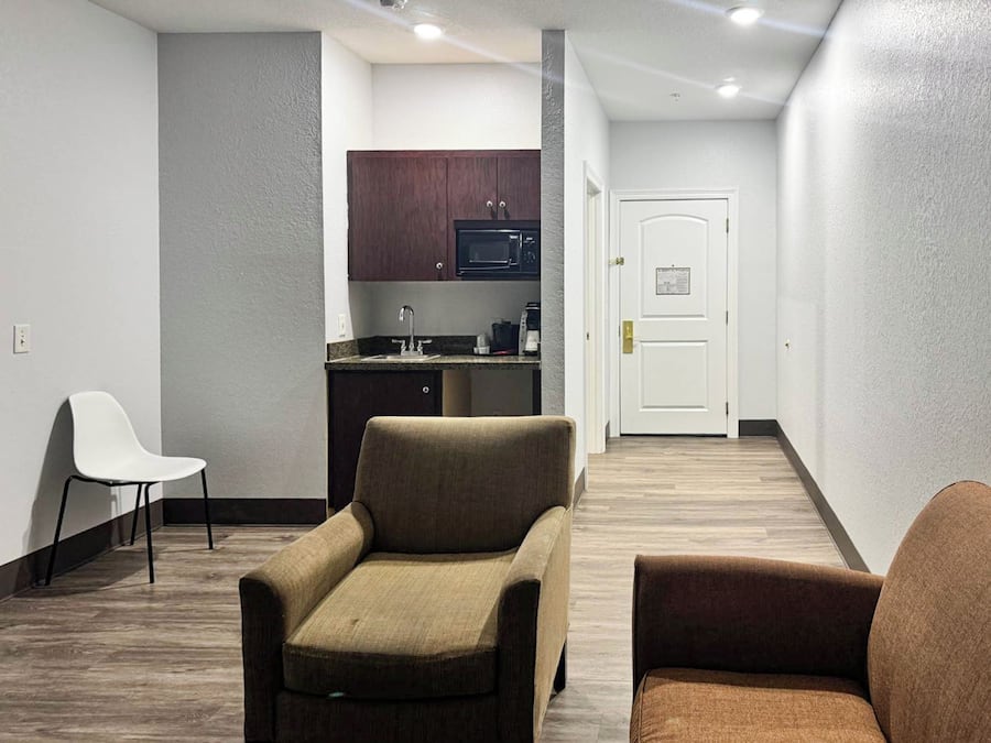 A hallway with a kitchenette, two armchairs, and a door.