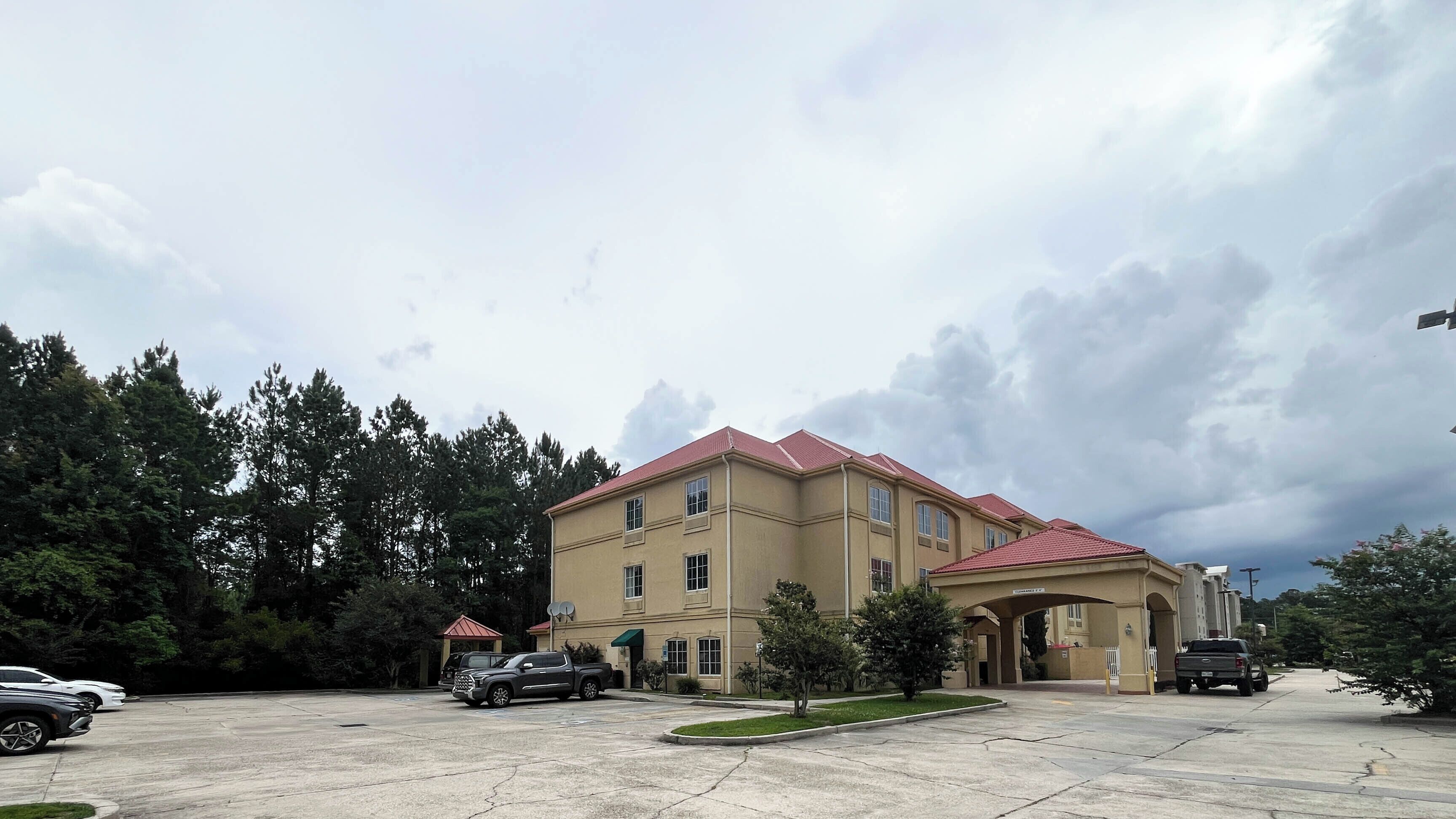 A large building with a red roof, multiple windows, and a parking lot with several cars.