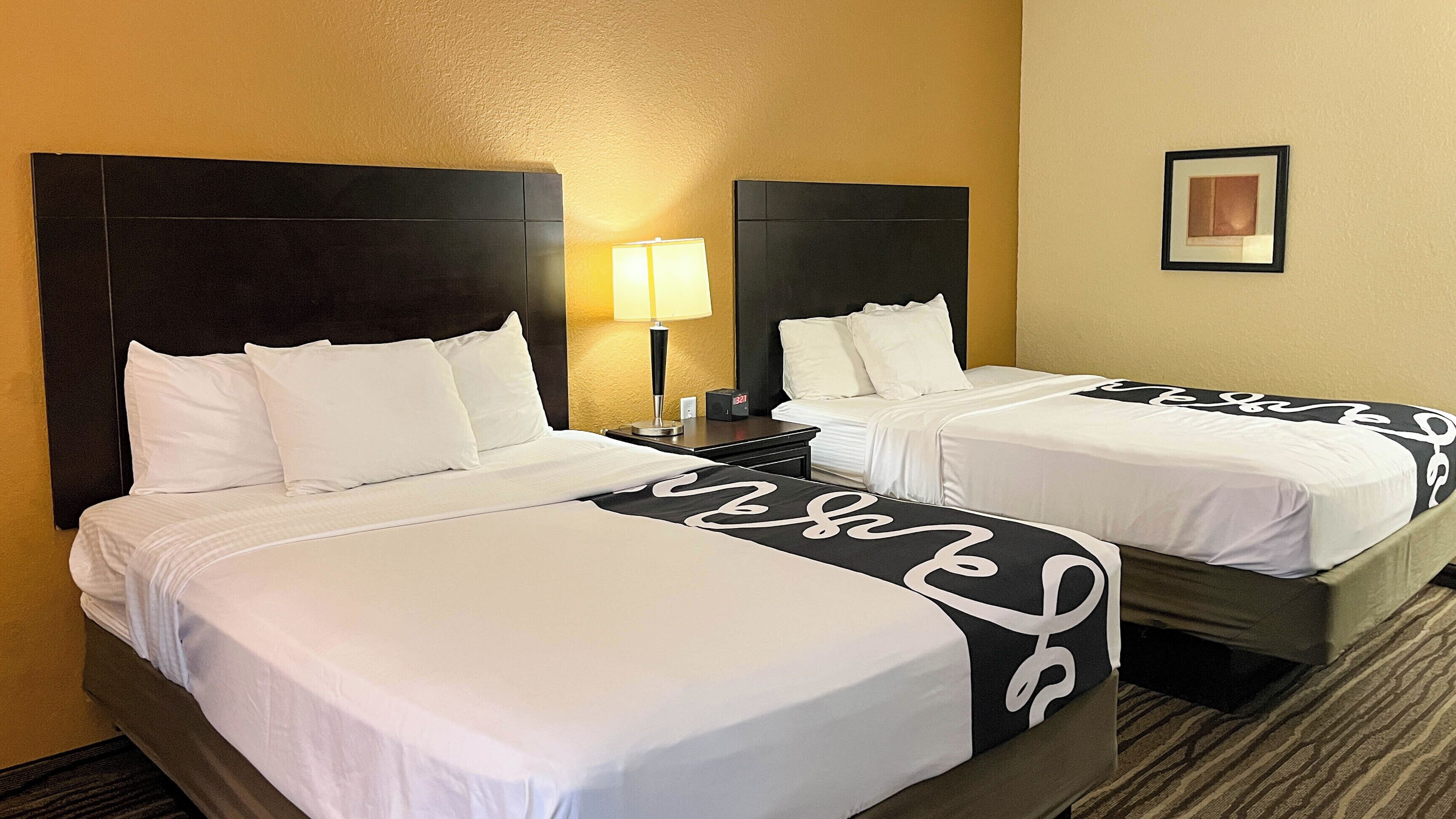 A hotel room with two beds, a nightstand with a lamp, and a framed picture on the wall.
