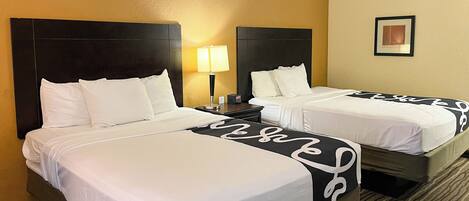 A hotel room with two beds, a nightstand with a lamp, and a framed picture on the wall.