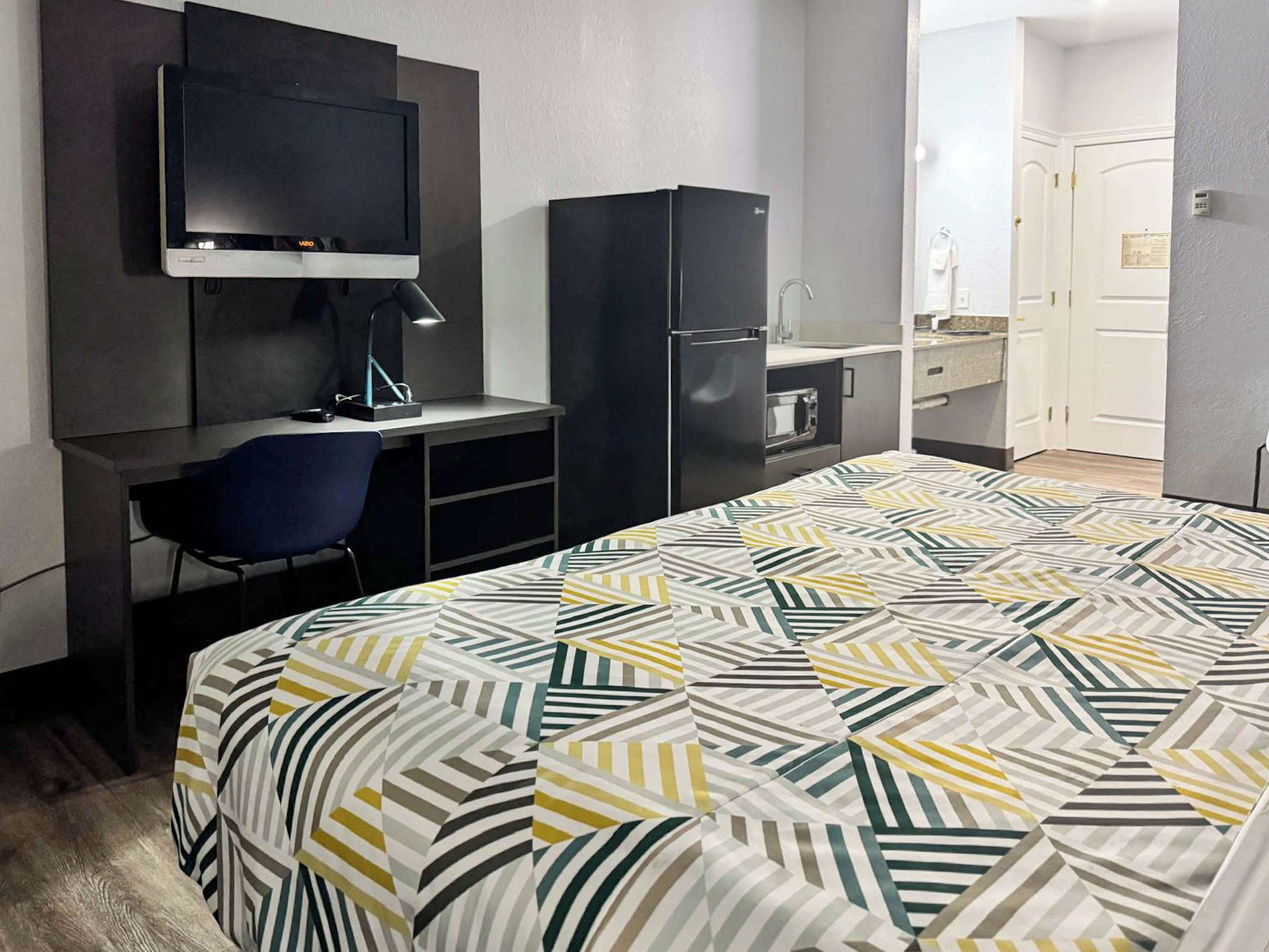 A hotel room with a bed, a desk with a chair, a television, a wardrobe, and a bathroom.