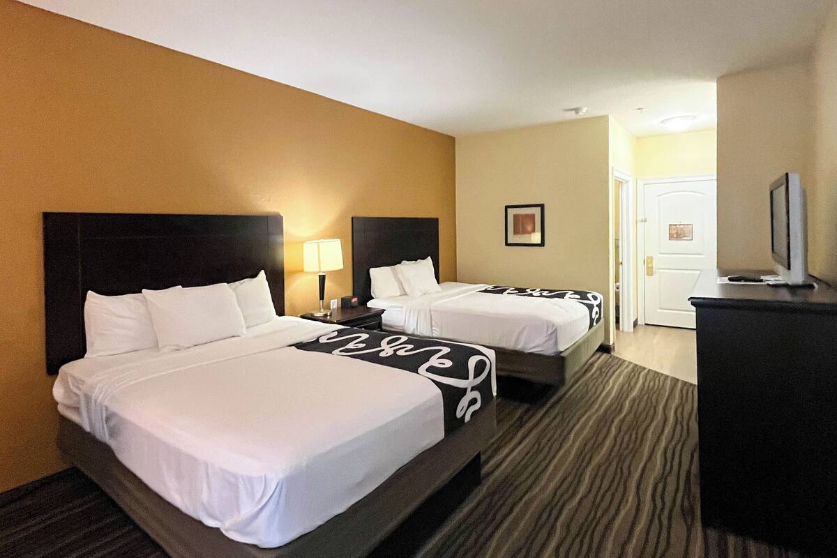 A hotel room with two beds, a TV, and a door.