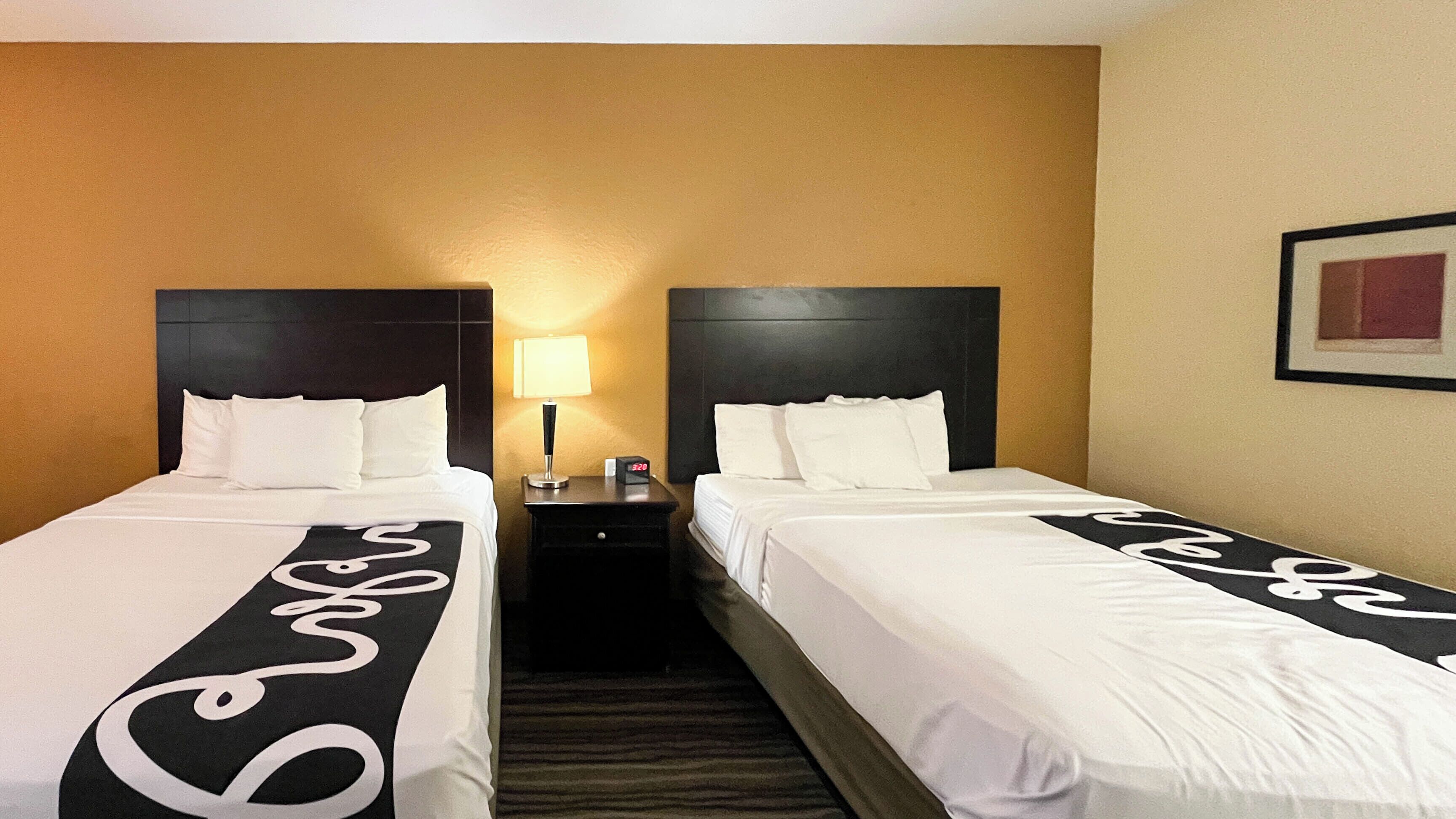 A hotel room with two beds, a nightstand with a lamp, and a framed picture on the wall.