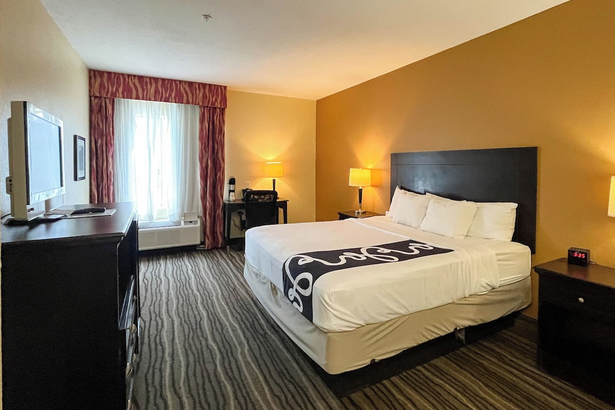 A hotel room with a bed, two bedside lamps, a desk with a computer, and a TV.