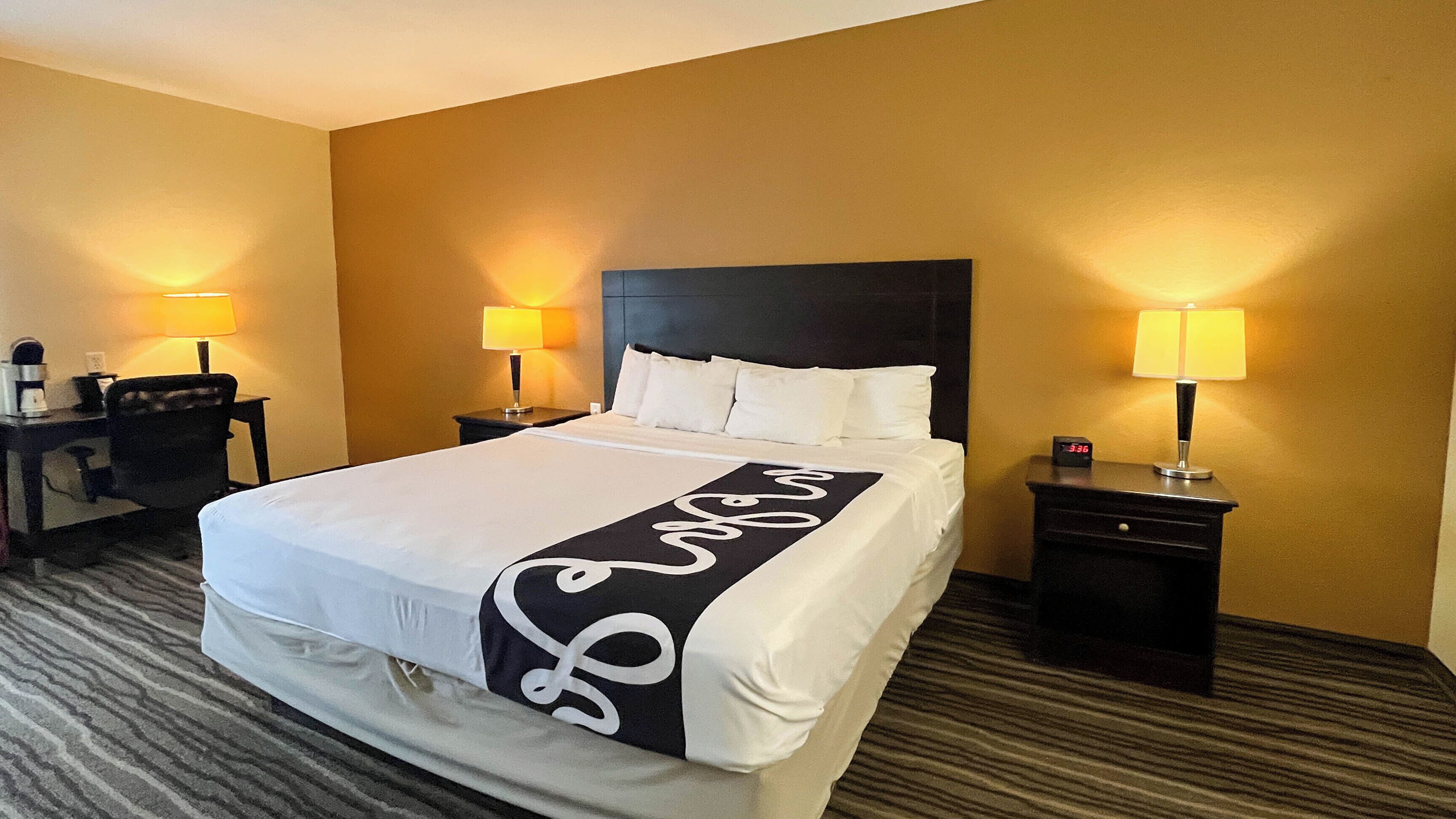Une chambre d’hôtel avec un grand lit, deux tables de chevet, un bureau et deux lampes.
