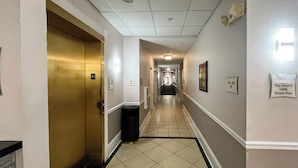 A hotel hallway with a gold elevator, a trash bin, and a sign indicating the hotel is 100% smoke-free.