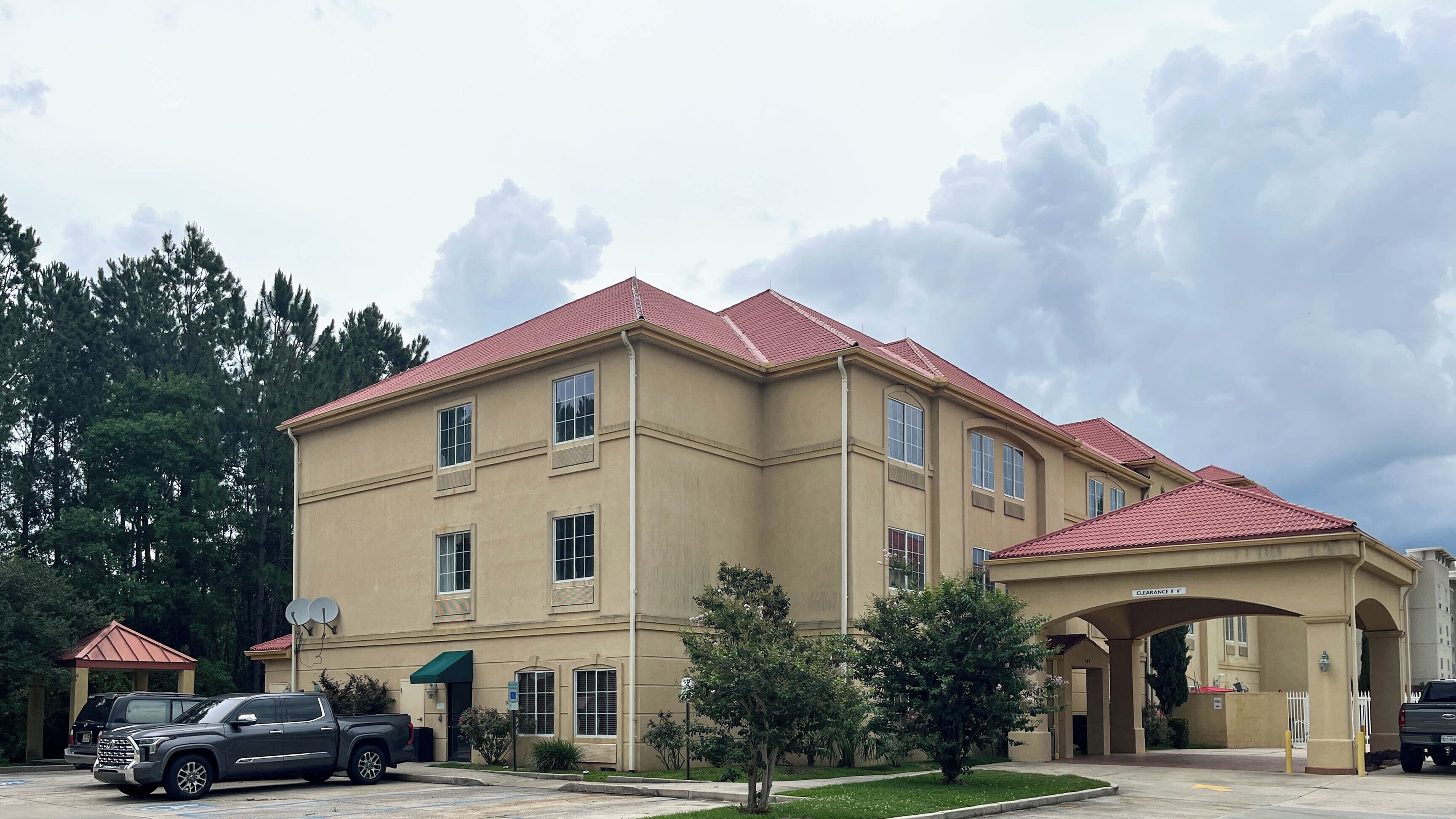 A multi-story building with a red-tiled roof, a covered entrance, and a parking area with vehicles.