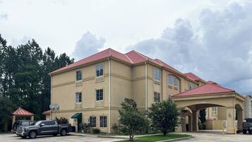 A multi-story building with a red-tiled roof, a covered entrance, and a parking area with vehicles.