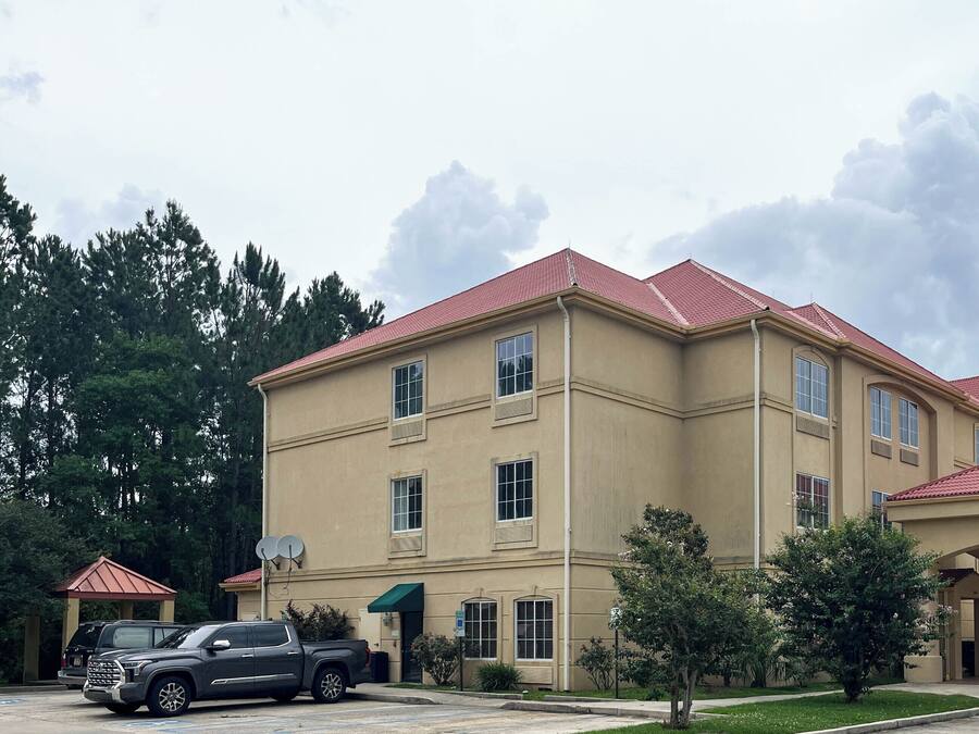 A multi-story building with a red-tiled roof, a covered entrance, and a parking area with vehicles.