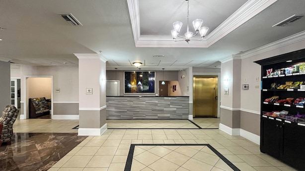 A hotel lobby with a reception desk, a vending machine, a wall-mounted light fixture, and a tiled floor.