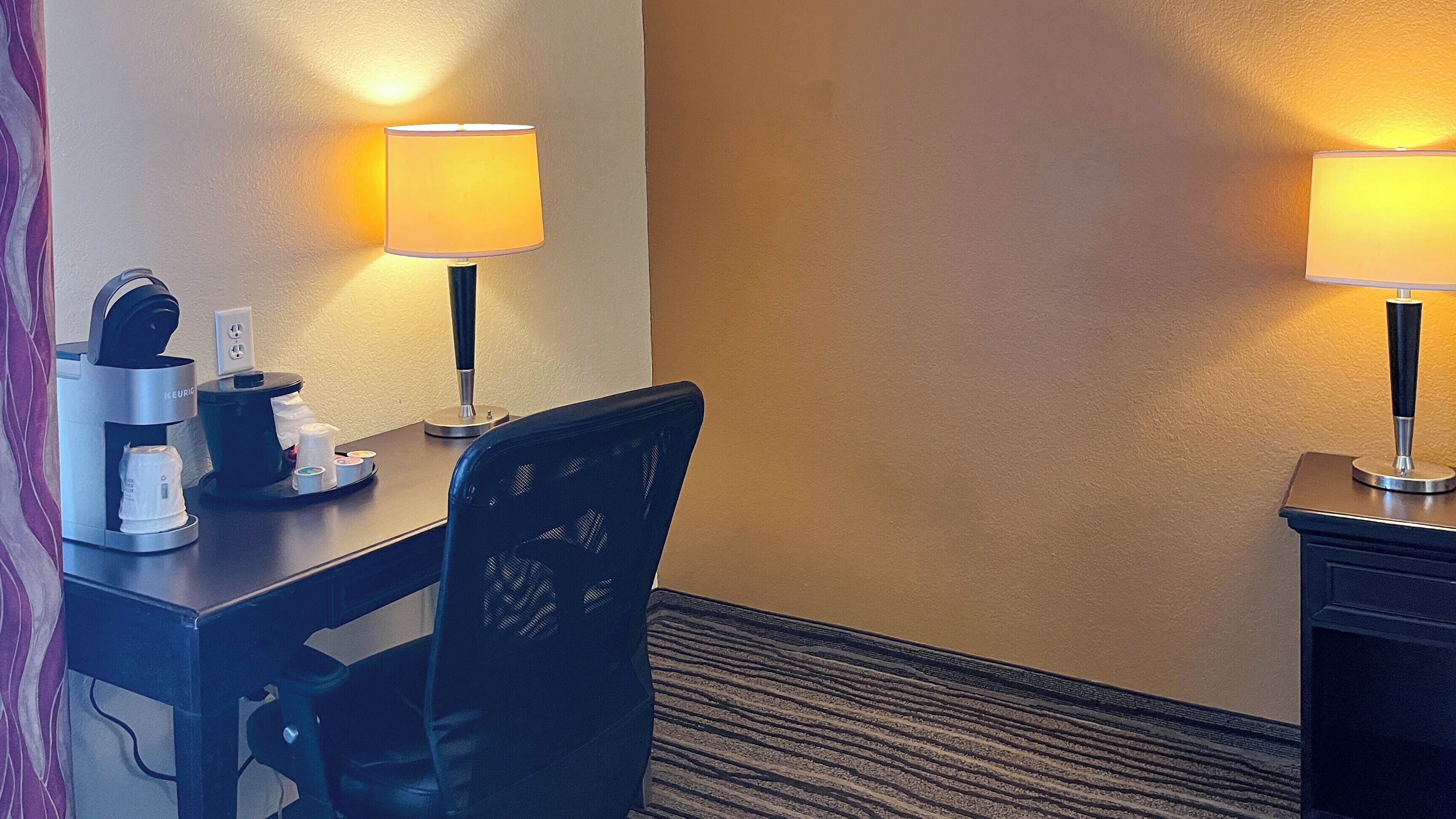 Une chambre d’hôtel équipée d’un bureau, d’une chaise, d’une machine à café, d’une lampe et d’un mur au revêtement texturé.