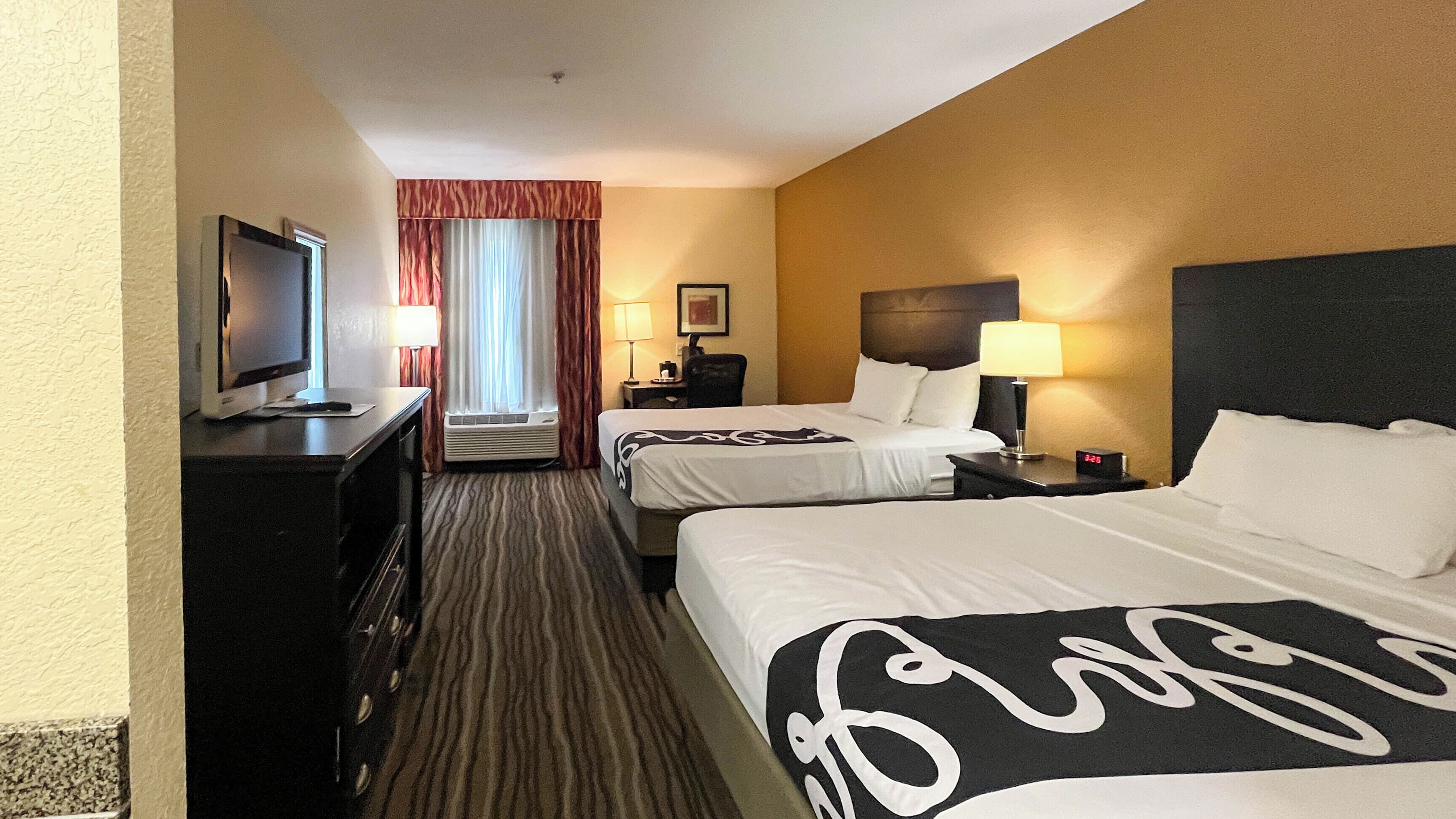 A hotel room with two beds, a TV, a desk, a lamp, and a clock.