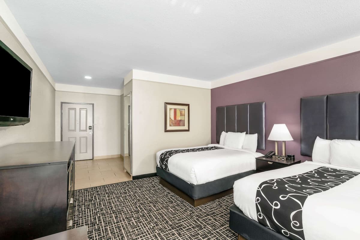 A hotel room with two beds, a desk, a TV, and a door.