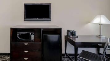 A hotel room with a flat-screen TV mounted on the wall, a minibar with a microwave, a coffee maker, and a desk with a chair.